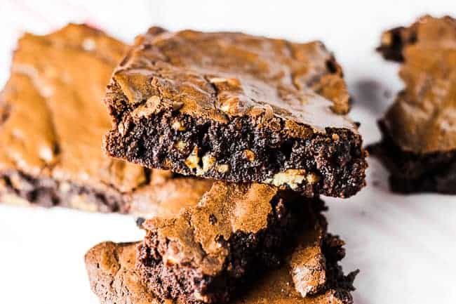 photo of fudgy chocolate brownie with walnuts and a shiny, crackly top. Brownie is stacked on top of other brownies.