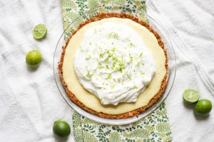 this is a key lime pie from above and it's covered in whipped cream. It's sitting in a clear, glass pie dish atop green and white tablecloths.