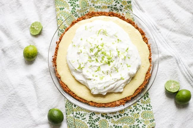 this is a key lime pie from above and it's covered in whipped cream. It's sitting in a clear, glass pie dish atop green and white tablecloths.