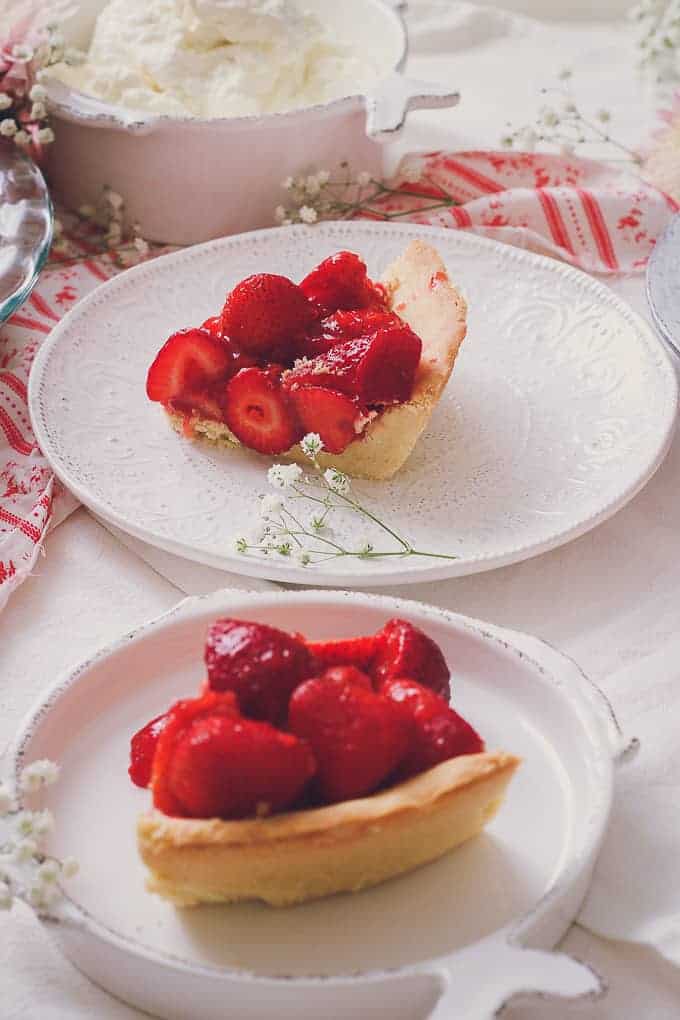 angled view of cut pieces of fresh strawberry pie and a bowl of whipped cream in background