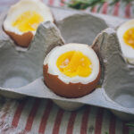 This is a photo at 45 degrees of 3 hard-boiled eggs in an egg carton, showcasing the bright orange, set yolk and set white.