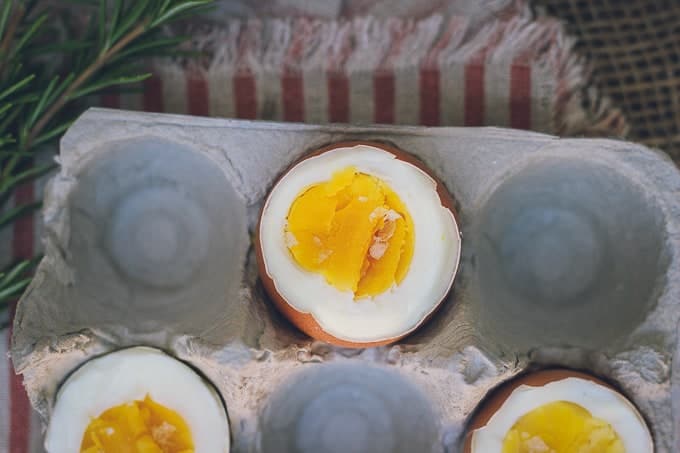 This is a photo of three hard-boiled eggs sitting in a cardboard egg carton, on top of a striped red and cream napkin. The eggs are shot from above and shows their set yolks and set whites.