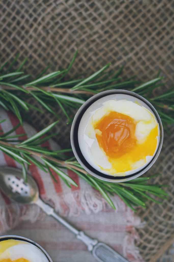 This is a photo of a soft-boiled egg shot from above. It's sitting in a small egg holder and the yolk is bright orange and jammy/runny and golden, with a set egg white surrounding it.
