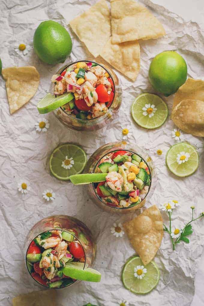 photo of three glasses filled to the brim with ceviche. there is lime, flowers, and chips decorating the shot.