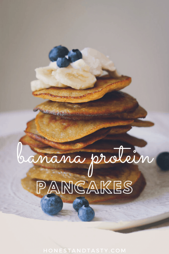 Pancake stack is shown from the side, sitting on a white plate and topped with whipped cream, banana slices, and blueberries.